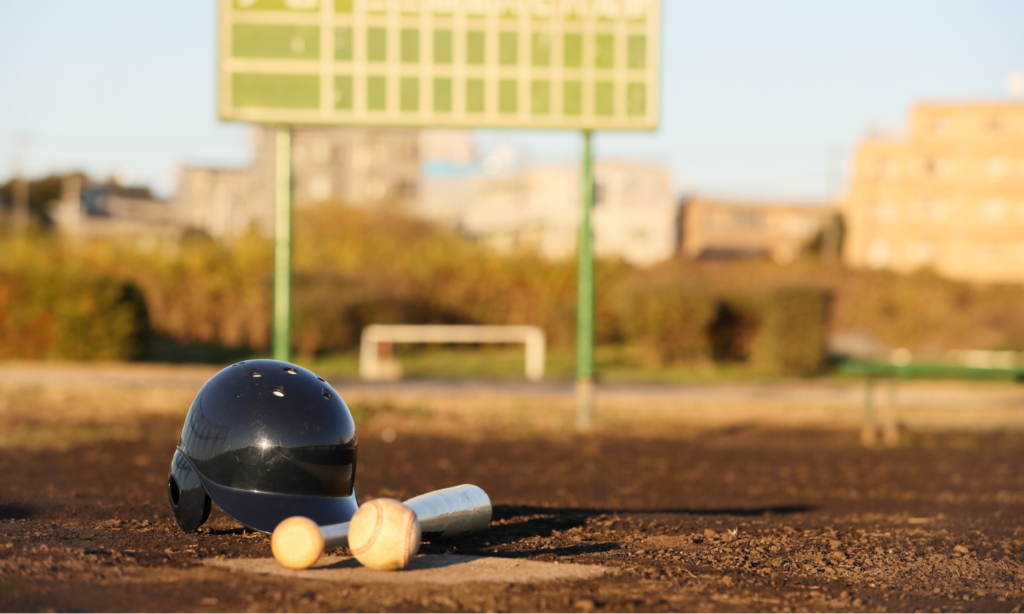 A baseball helmet, ball, and bat on a plate with the ballfield in the background, representing a spring day trip from The Station RV Resort.