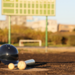 A baseball helmet, ball, and bat on a plate with the ballfield in the background, representing a spring day trip from The Station RV Resort.