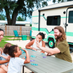 Family enjoying a summer staycation at The Station RV Resort in Madison, Florida while playing a game at a picnic table outside their RV campsite.