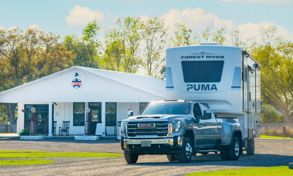 GMC truck towing a fifth-wheel RV in front of The Station RV Resort in Madison, Florida, a convenient stop for snowbird travelers along I-10 and I-75.